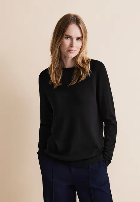 Frau mit schwarzen Pullover und dunkelblauer Hose vor beigem Hintergrund.